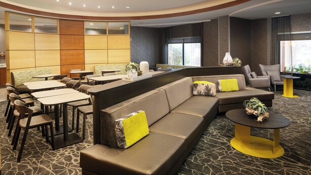 A modern hotel lobby with a curved seating area, multiple tables, and a large sofa with yellow cushions. - SpringHill Suites by Marriott Savannah I-95 (Savannah)