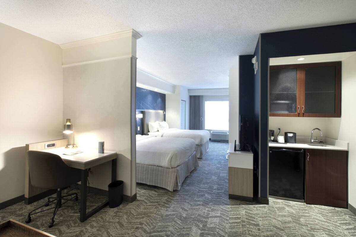 Habitación de hotel con escritorio, dos camas, kitchenette y un amplio ventanal.