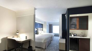 Une chambre d’hôtel équipée d’un bureau, de deux lits, d’une kitchenette et d’une grande fenêtre.