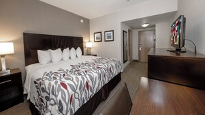 A hotel room with a large bed, bedside tables, a desk, and a television. - Red Roof Inn & Suites Newburgh – Stewart Airport/ West Point (New Windsor)