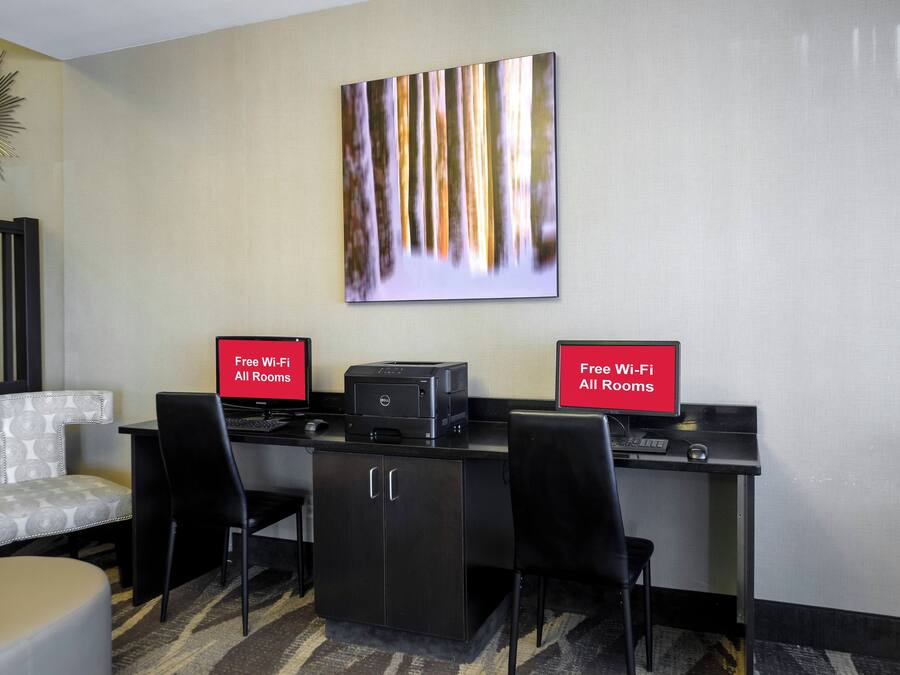 Habitación de hotel con escritorio, dos sillas, una impresora y un cartel que indica Wi-Fi gratuito en todas las habitaciones.