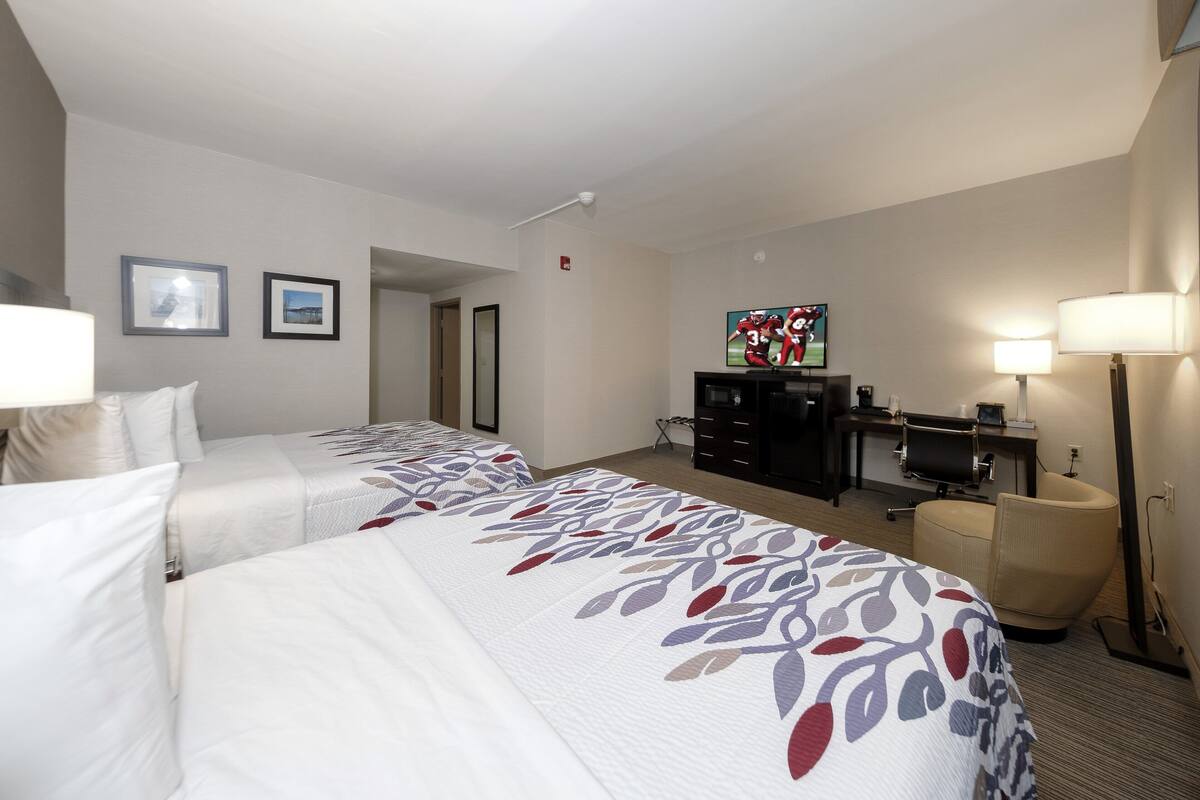 Habitación de hotel con dos camas, un escritorio, una silla, un televisor y una lámpara.