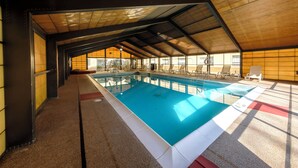 An indoor swimming pool with a tiled floor, surrounded by lounge chairs and a high, sloped ceiling. - Red Roof Inn & Suites Newburgh – Stewart Airport/ West Point (New Windsor)