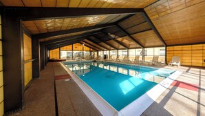 An indoor swimming pool with a tiled floor, surrounded by lounge chairs and a high, sloped ceiling. - Red Roof Inn & Suites Newburgh – Stewart Airport/ West Point (New Windsor)