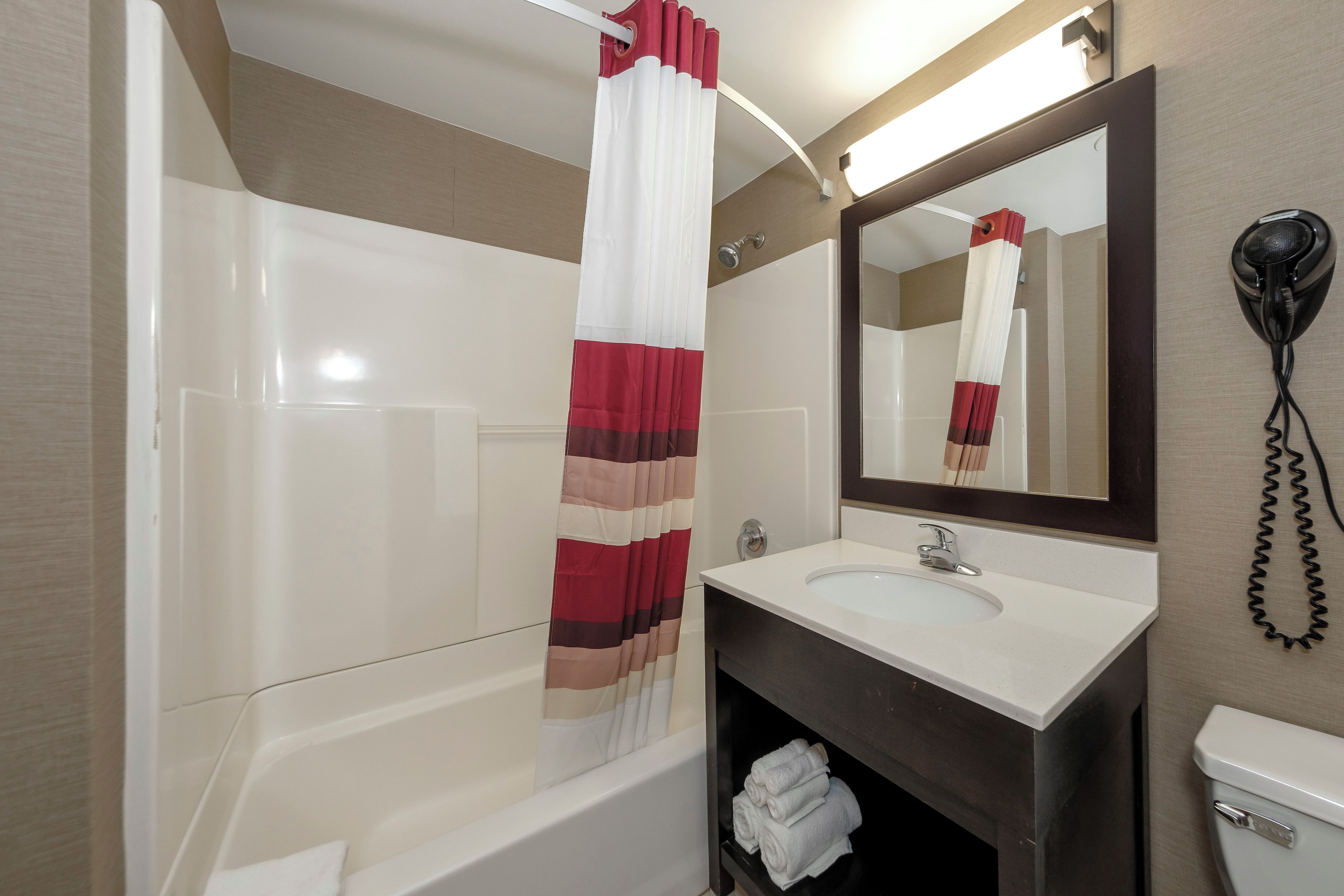 A bathroom with a bathtub, a sink, a mirror, and a hairdryer.