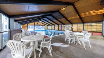 Un área de piscina interior con techo cubierto, varios espacios de descanso y vistas al exterior.