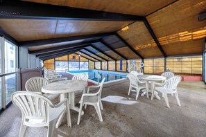 Un espace piscine intérieur doté d’un toit couvert, de plusieurs coins salon et offrant une vue sur l’extérieur.