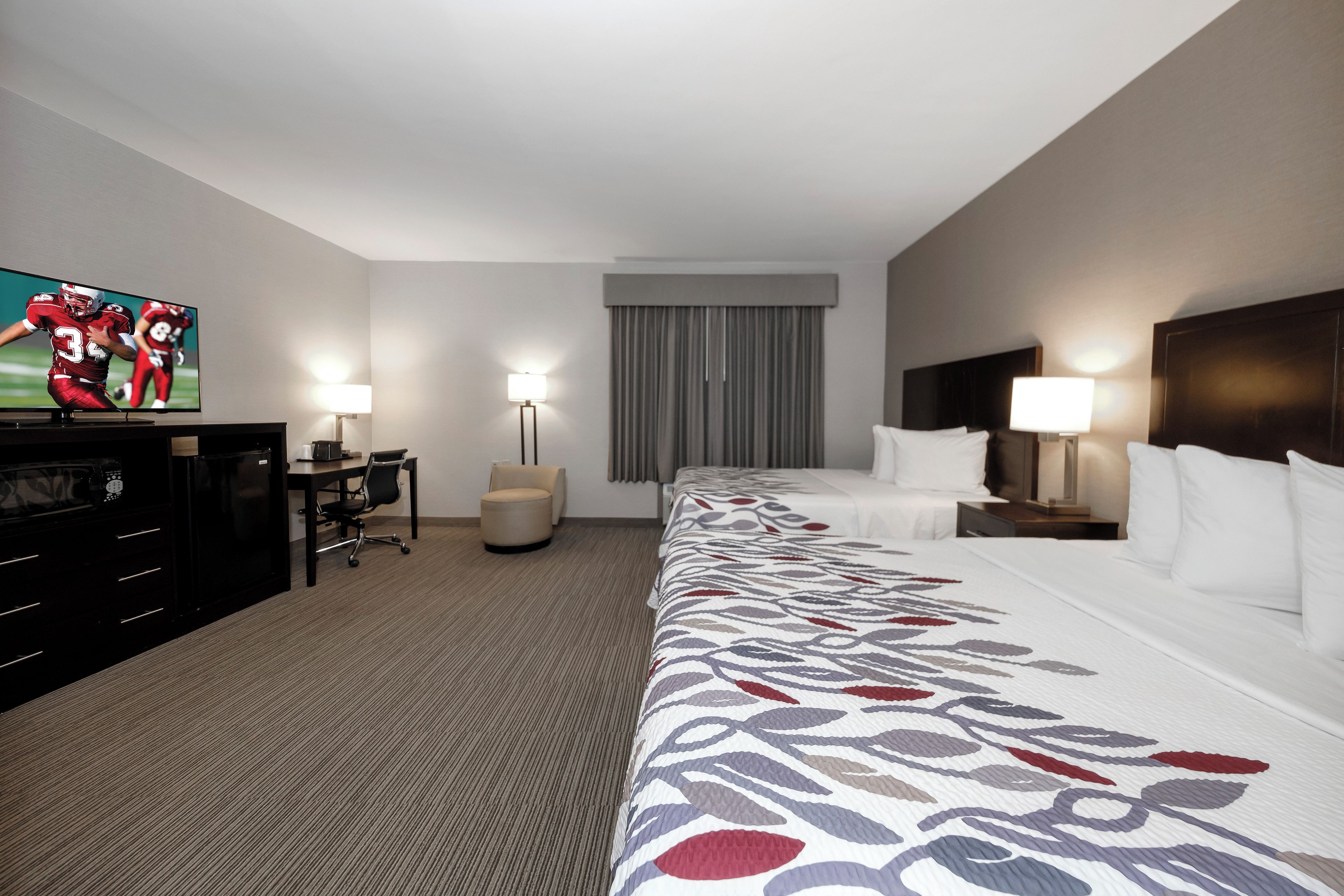 Habitación de hotel con cama, escritorio, silla, televisión y ventana con cortinas.