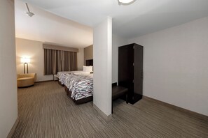A hotel room with a bed, a desk, a chair, a wardrobe, and a lamp. - Red Roof Inn & Suites Newburgh – Stewart Airport/ West Point (New Windsor)