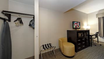 Una camera d'albergo con un letto, una televisione, un tavolino, una sedia e un attaccapanni con alcuni capi appesi.
