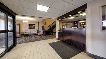 A hotel lobby with a reception desk, a sofa, a staircase, and a patterned carpet.