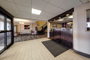 Un hall de hotel con una recepción, un sofá, una escalera y una alfombra estampada.