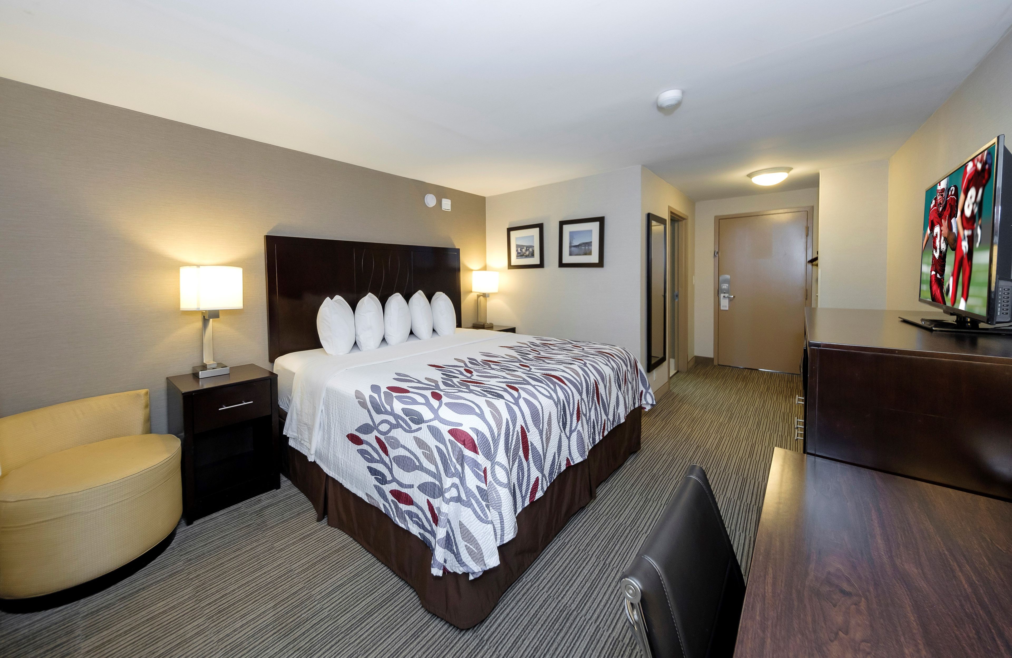 A hotel room with a large bed, bedside lamps, a desk, a chair, and a television.