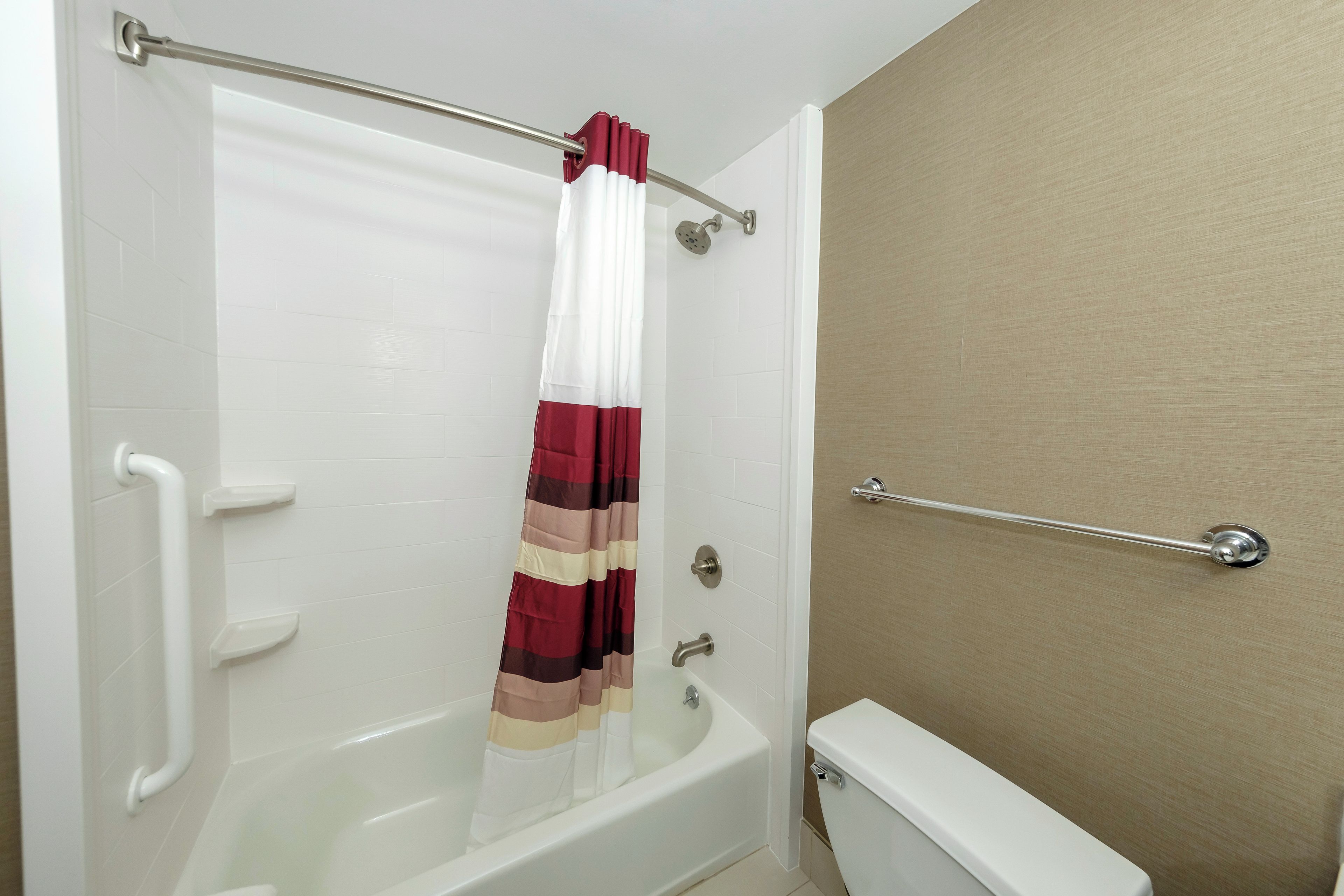 A bathroom with a white bathtub, a red and white striped shower curtain, and a beige wall.