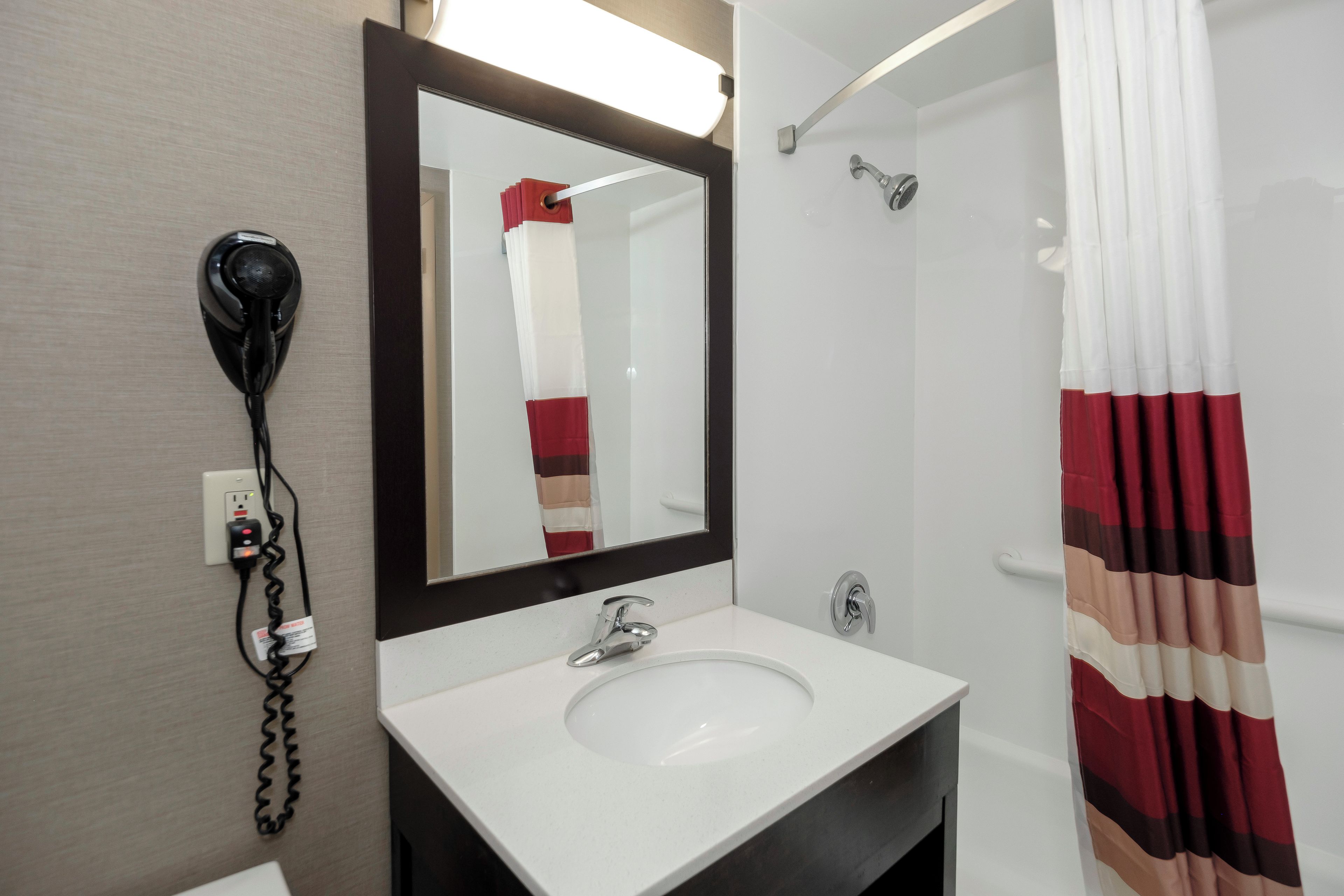 Un baño con lavamanos blanco, espejo, secador de pelo y cortina de ducha.