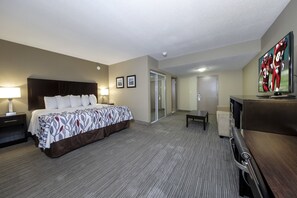 A hotel room with a large bed, a desk, a TV, and a door leading to another room. - Red Roof Inn & Suites Newburgh – Stewart Airport/ West Point (New Windsor)