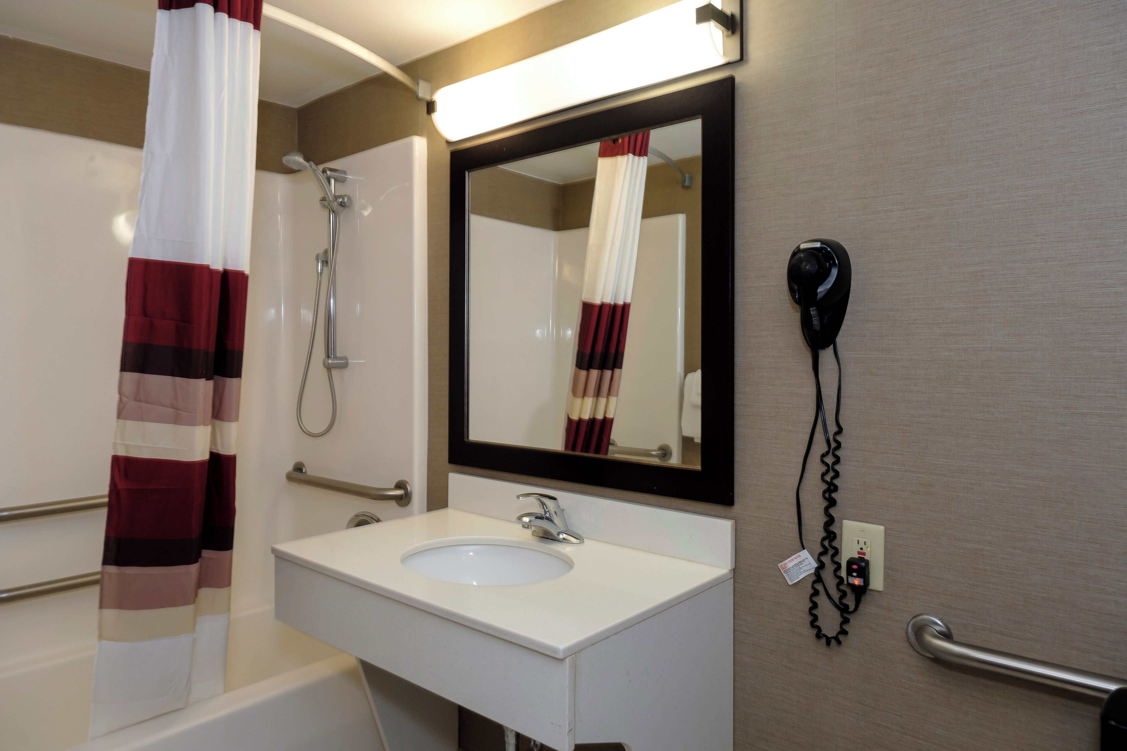 Une salle de bain avec un lavabo blanc, un miroir, une douche et un sèche-cheveux fixé au mur.