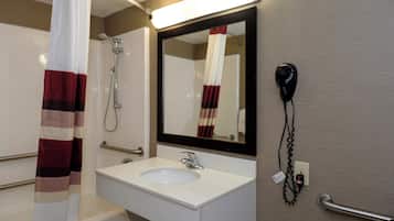 Une salle de bain avec un lavabo blanc, un miroir, une douche et un sèche-cheveux fixé au mur.