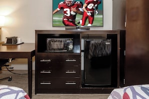 Habitación de hotel con televisión de pantalla plana montada en un mueble de madera, microondas y refrigerador.