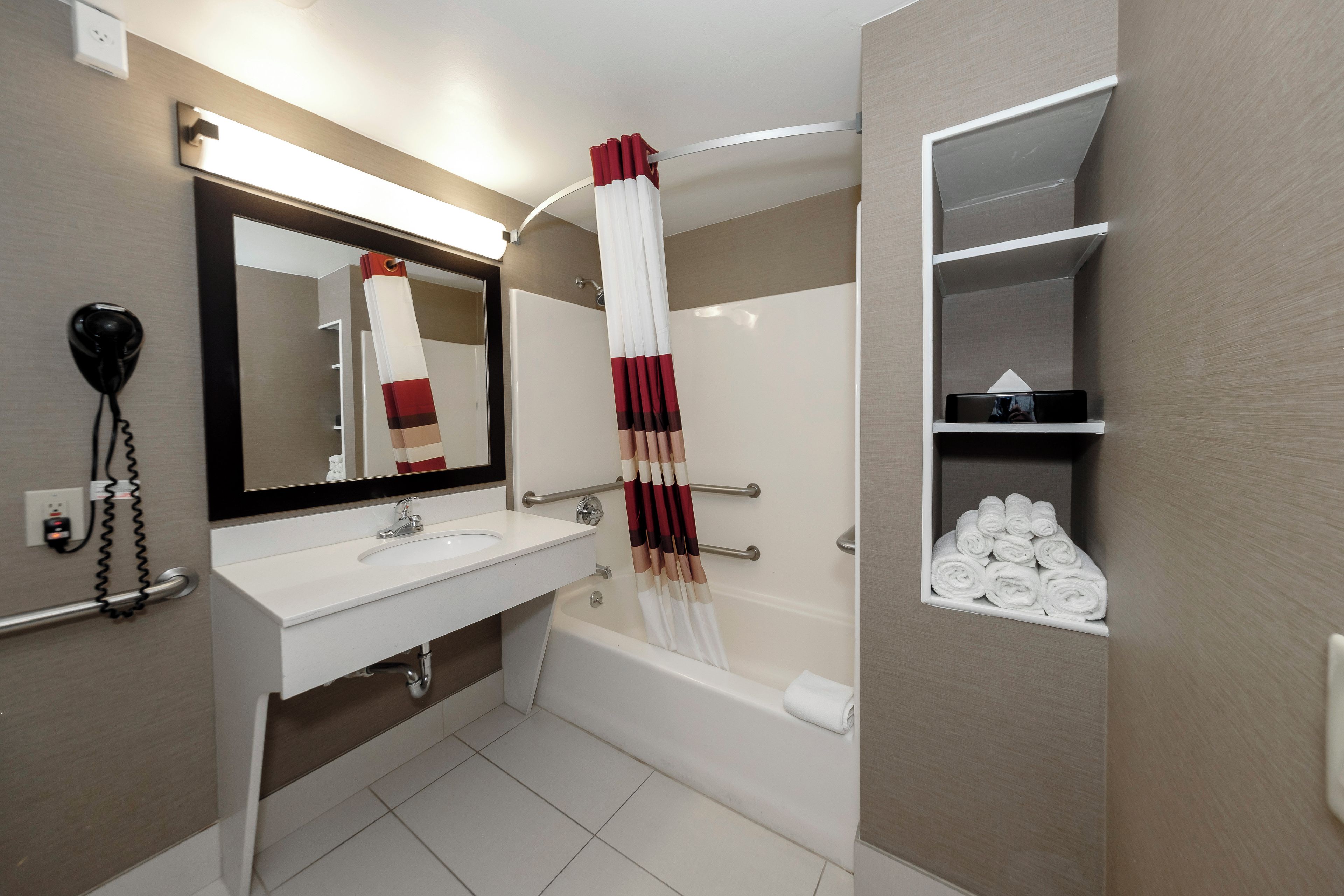 A modern bathroom with a white sink, a large mirror, a towel rack, and a shelf with neatly folded towels.