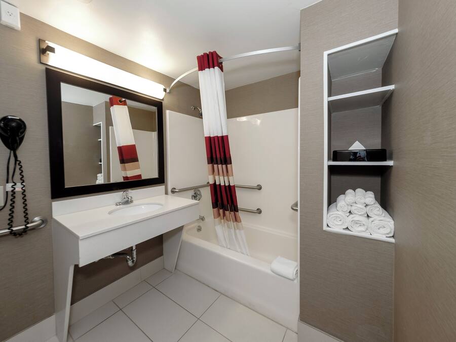 A modern bathroom with a white sink, a large mirror, a towel rack, and a shelf with neatly folded towels.