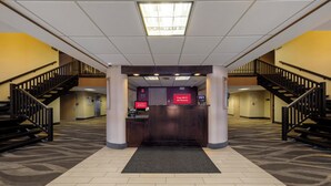A hotel lobby with a reception desk, two staircases, and a carpeted floor. - Red Roof Inn & Suites Newburgh – Stewart Airport/ West Point (New Windsor)