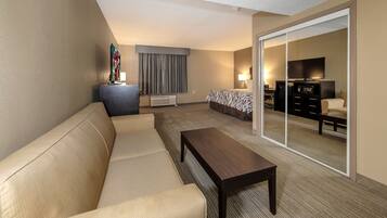A hotel room with a sofa, a small table, a TV, a desk with a chair, and a bed.