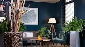 Un área de estar moderna con una pared azul oscuro, un mapa, una lámpara y varias plantas en macetas.