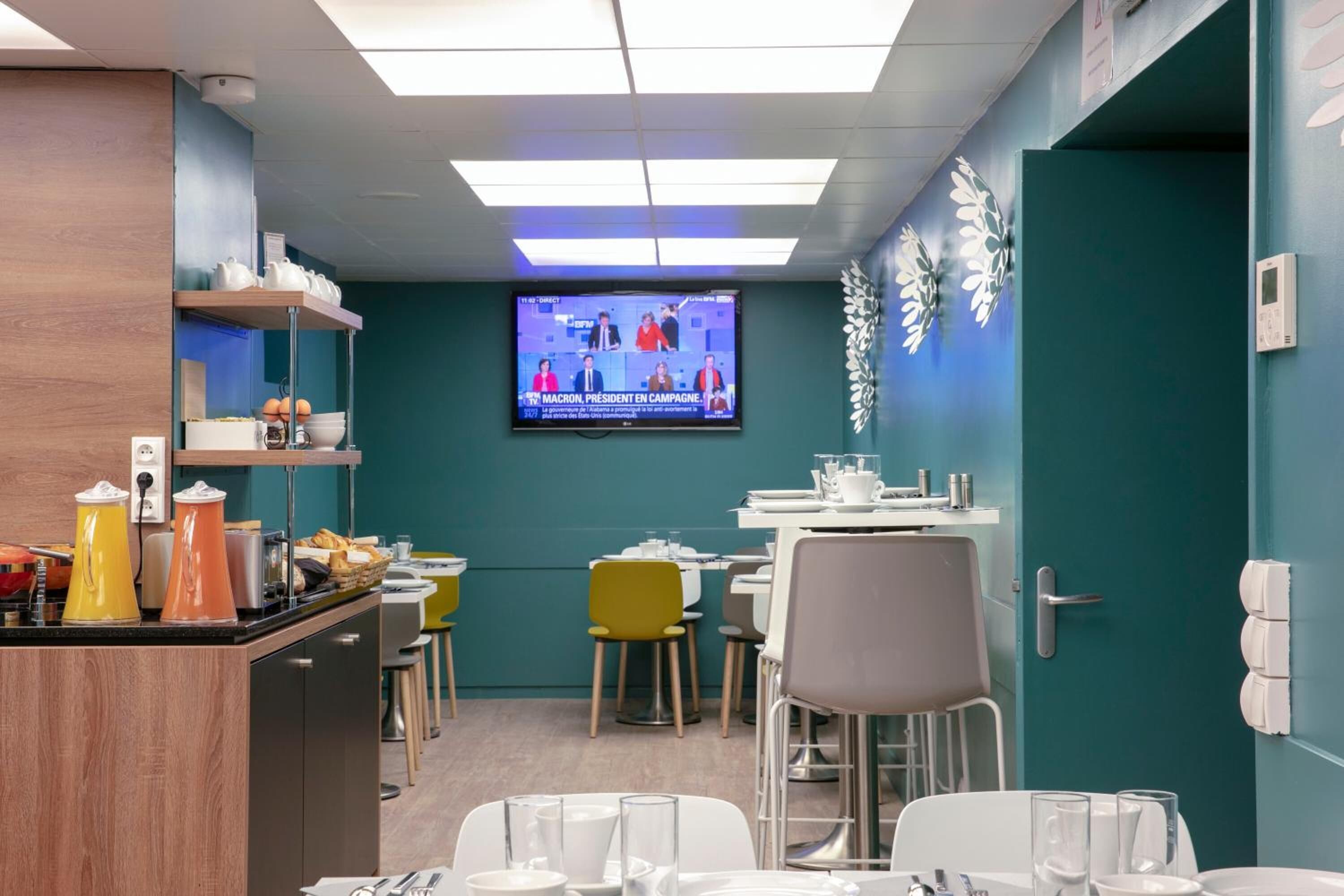A modern dining area with a television displaying a news broadcast, a buffet counter with food items, and a seating arrangement with chairs and tables.