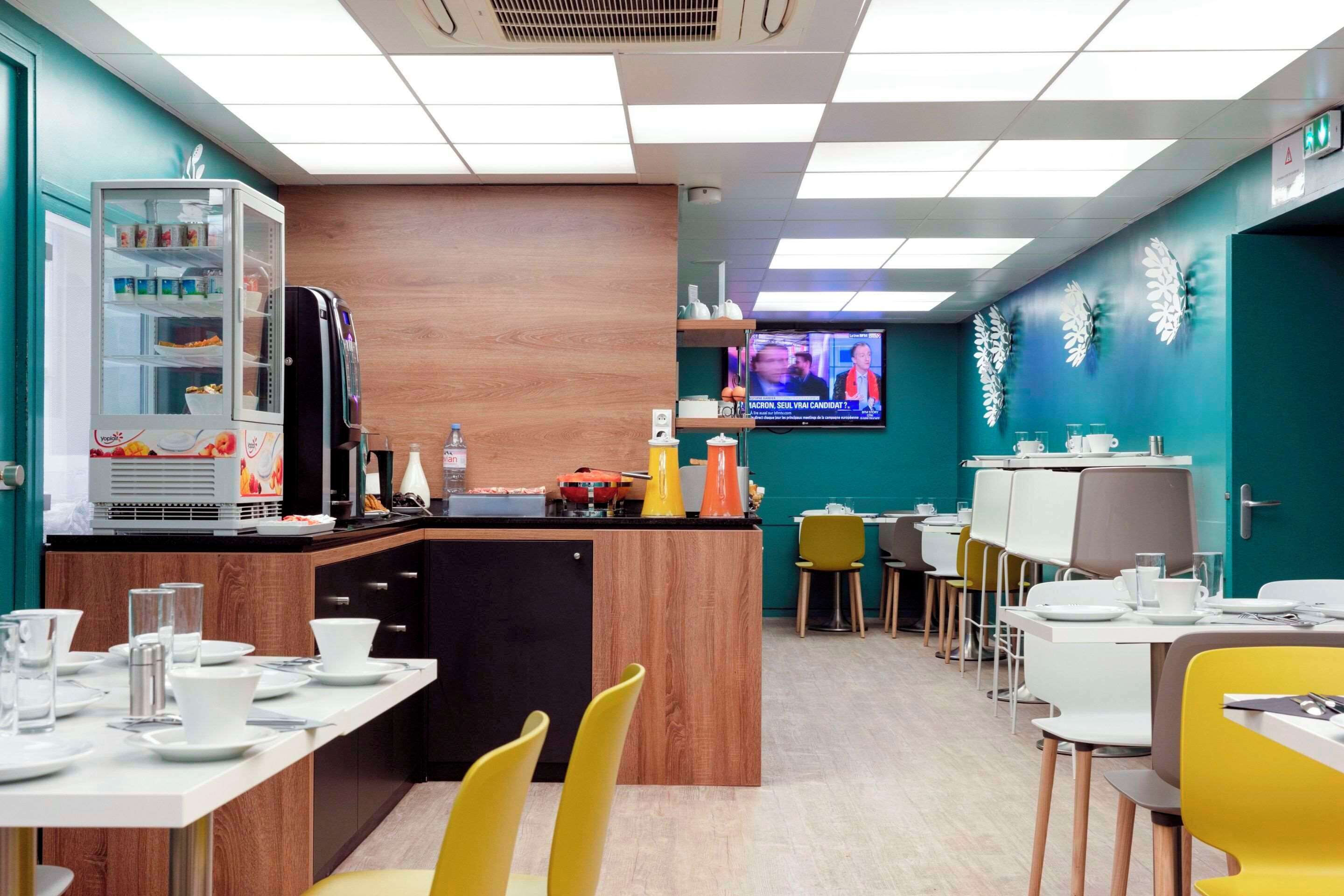 Un ristorante moderno con un bancone centrale, diversi tavoli e sedie. Sullo sfondo, uno schermo televisivo mostra un notiziario.