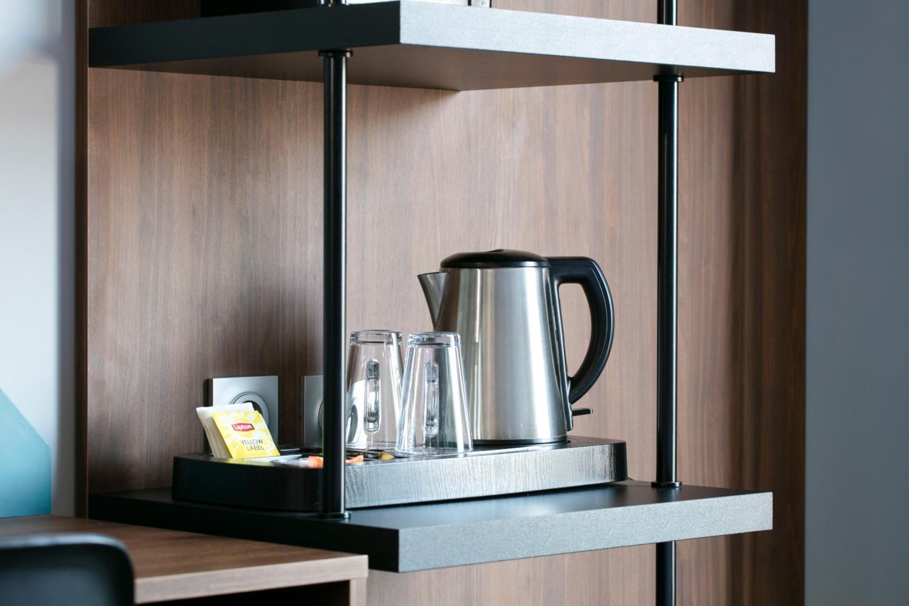 A kitchen area with a coffee maker, two glasses, and a packet of coffee on a shelf.