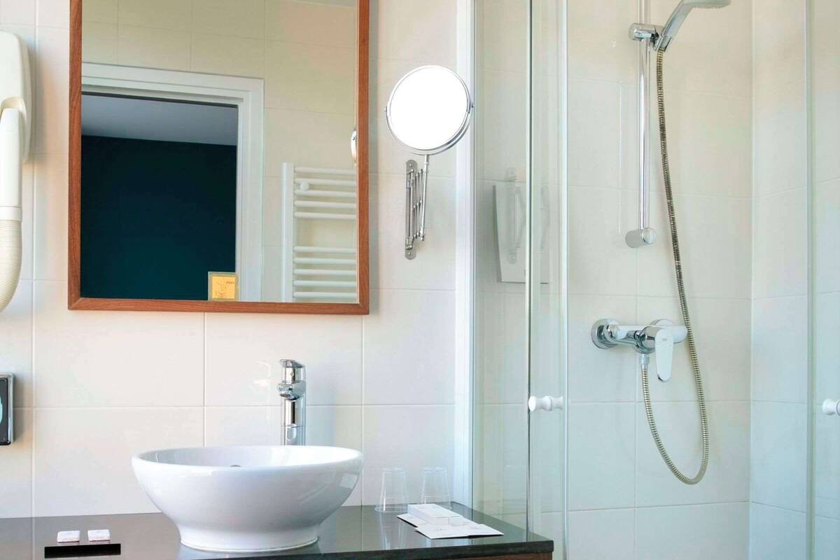 A modern bathroom with a glass-enclosed shower, a white sink, a mirror, and a towel rack.
