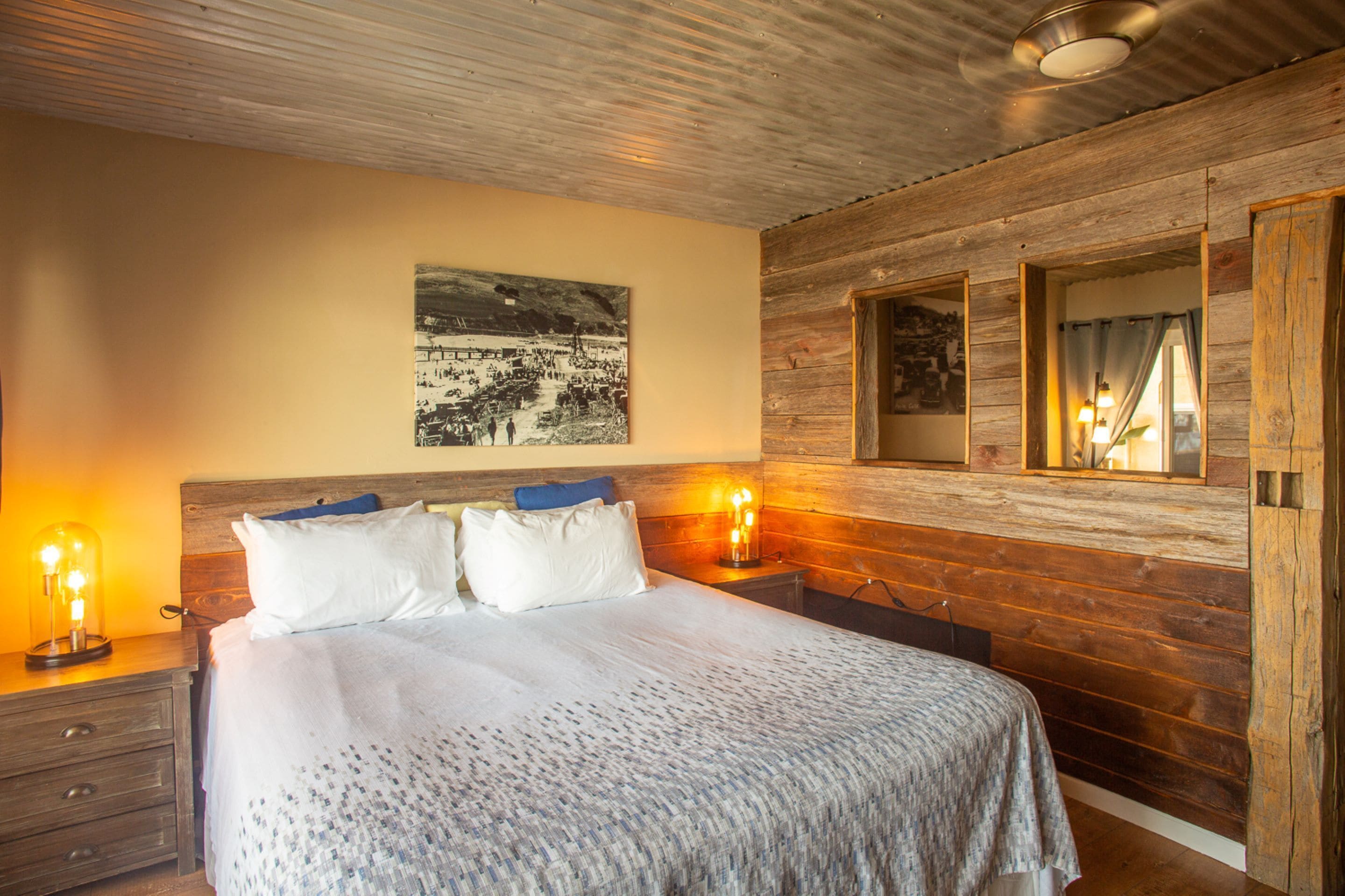Une chambre à coucher avec une tête de lit en bois, un lit recouvert de draps blancs, deux lampes de chevet et un tableau encadré accroché au mur.