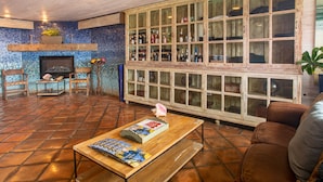 A spacious living room with a tiled floor, a wooden coffee table with magazines, a fireplace, and a large cabinet with glass doors. - Inn at Avila Beach (Avila Beach)