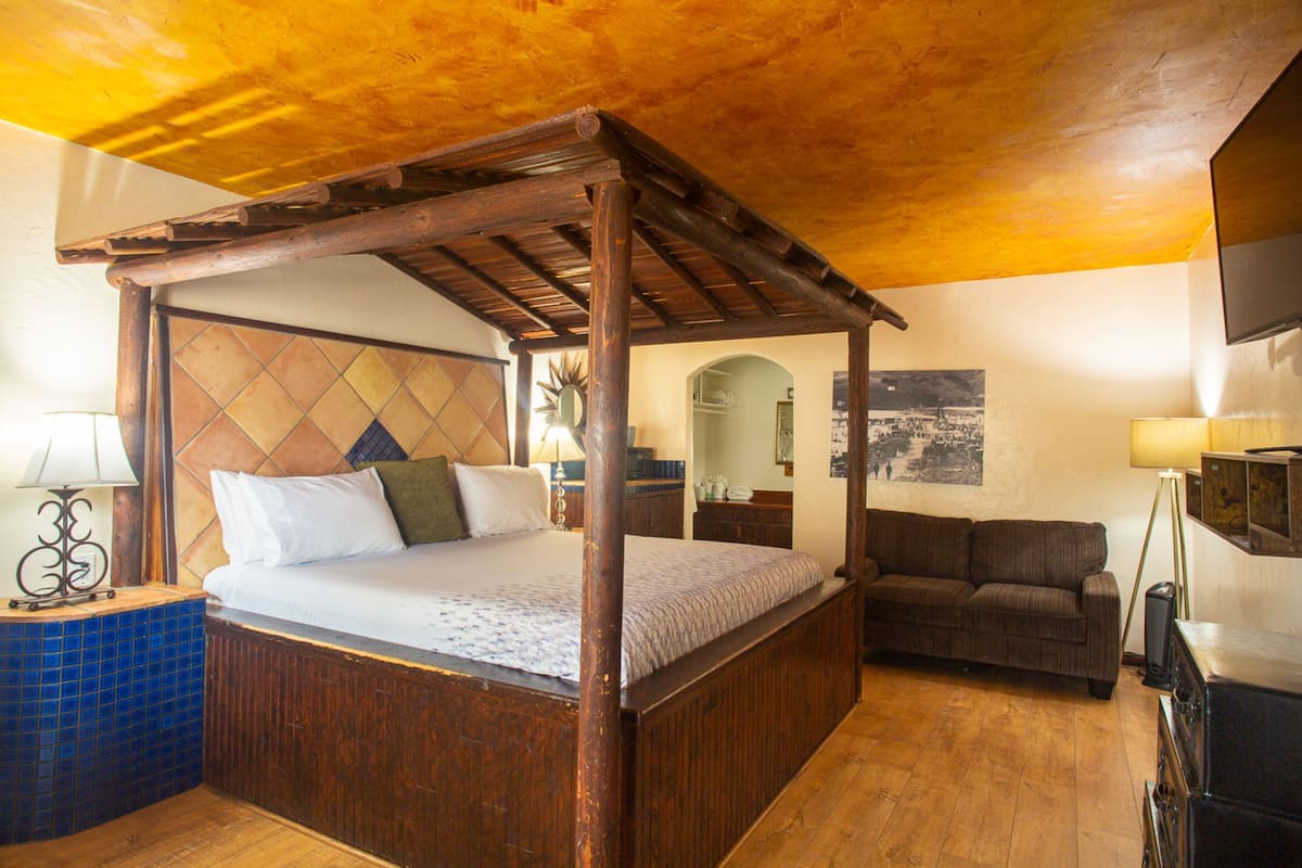 A room with a wooden four-poster bed, a sofa, a small table, and a television.