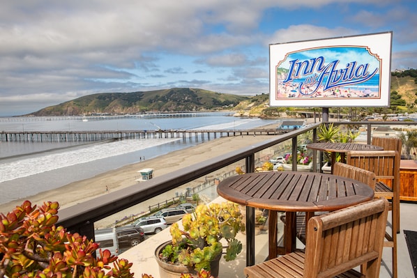 A beachside view with a sign for 'Inn at Avila' and wooden deck furniture overlooking the ocean.