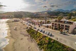 A coastal hotel with a parking lot, beach access, and a view of the ocean and hills.