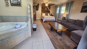 A hotel room with a large bathtub, a wooden floor, a bed with a white bedspread, a brown sofa, and a ceiling fan. - Inn at Avila Beach (Avila Beach)