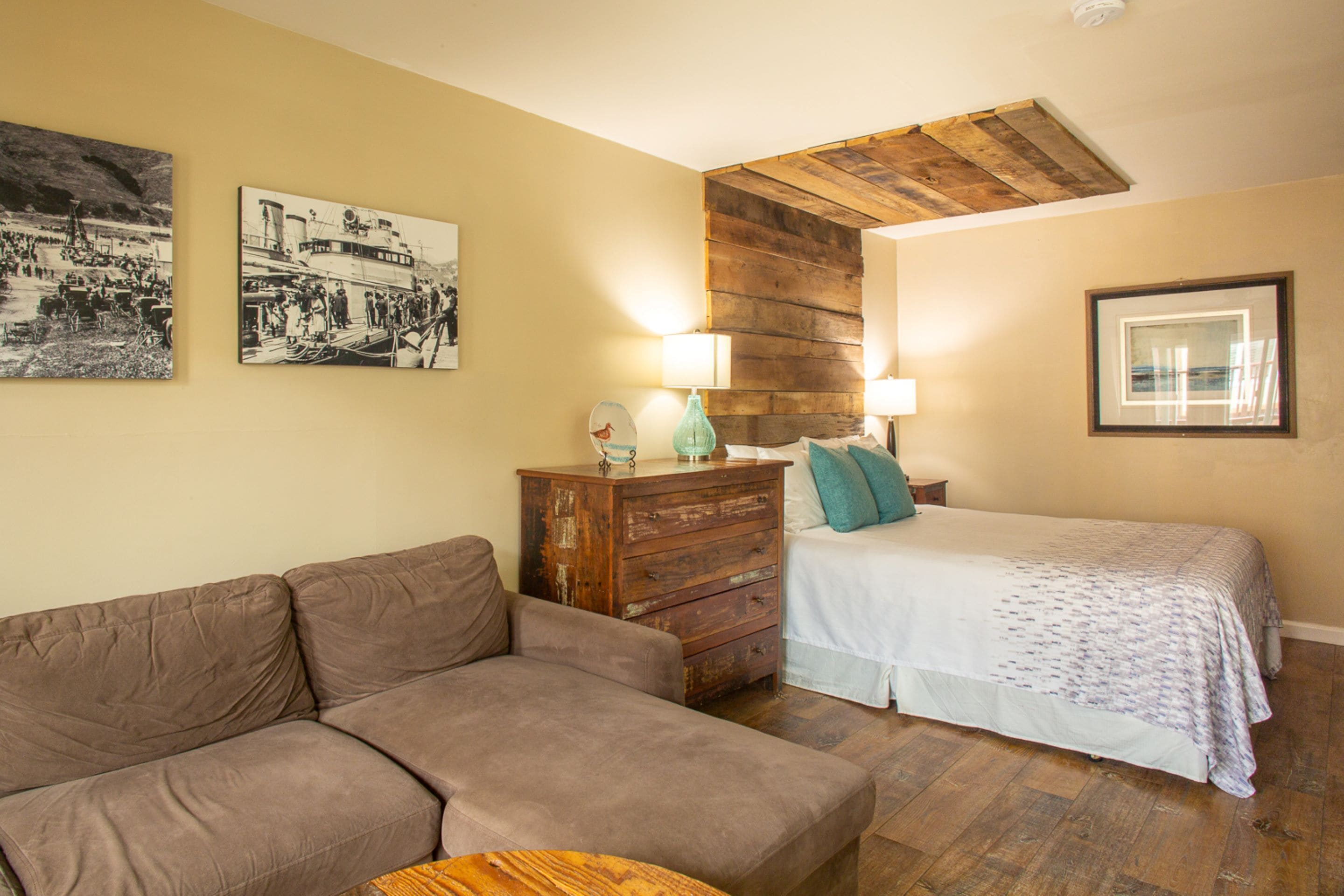 A cozy room with a brown sofa, a wooden dresser, a bed with a white bedspread, and two wall-mounted lamps.