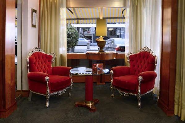A room with two red upholstered chairs, a round glass table, and a decorative vase.