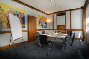 Un salón de conferencias con una gran mesa, sillas negras, una pizarra y dos cuadros en las paredes.