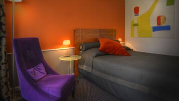 Een hotelkamer met een bed, een paarse fauteuil, een klein rond tafeltje en een kunstwerk aan de muur.