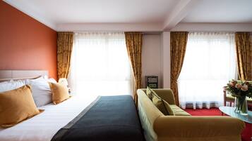 Una habitación de hotel con una cama, un sofá, una mesita con un florero y un tablero de ajedrez sobre una mesita de noche.
