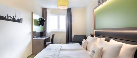 Una habitación de hotel con cama, escritorio, silla, televisor y ventana con cortinas.
