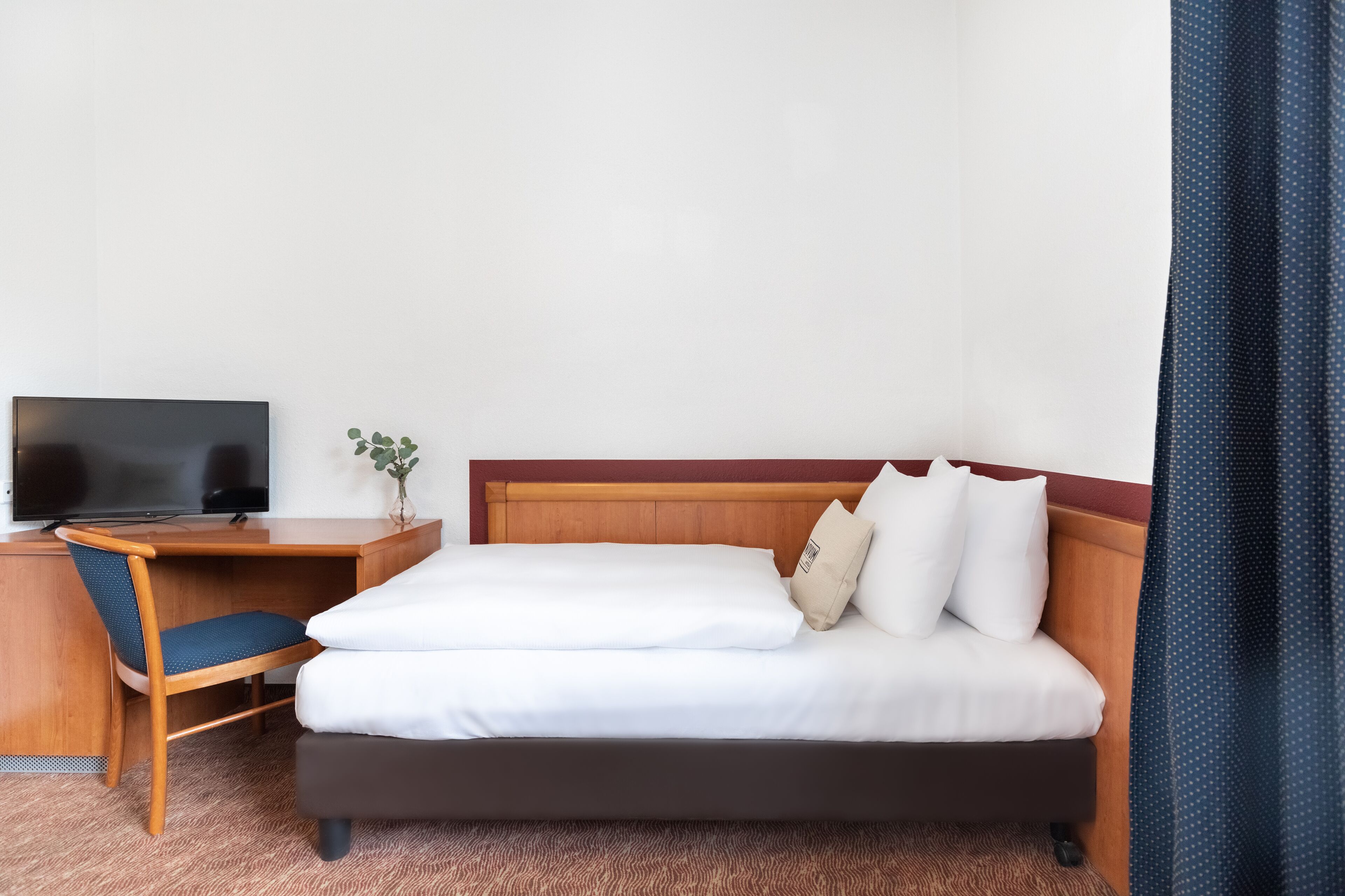 Ein Hotelzimmer mit Bett, Schreibtisch mit Fernseher, Stuhl und einer kleinen Pflanze.