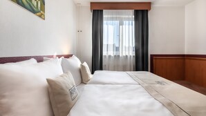Habitación de hotel con una cama grande, cabecera de madera, un cuadro en la pared y una ventana con cortinas.