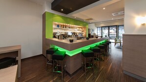 Un área de bar moderna con mostrador de madera, taburetes verdes y un interior bien iluminado.