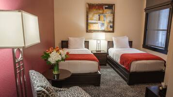 A hotel room with two beds, a sofa, a table with a vase of flowers, and a painting on the wall.