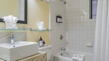 Une salle de bain avec un lavabo en marbre, une étagère en verre où sont posées des serviettes, une baignoire et un espace douche.