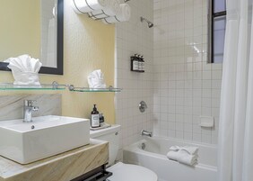 A bathroom with a marble sink, a glass shelf with towels, a bathtub, and a shower area.